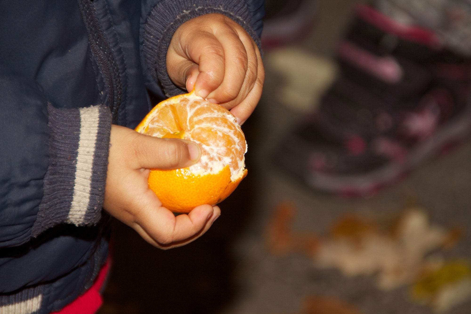 小小孩站在外面 穿蓝冬大衣 双手握着克隆橙